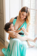 © oksana_bondar - A Mother breastfeeding her little baby girl in her arms sitting on window sill