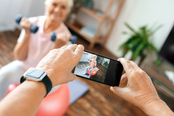 Wall Mural - Senior couple exercise together at home taking pictures on exercise ball close-up