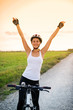 smiling girl on a bicycle with her hands up at sunset