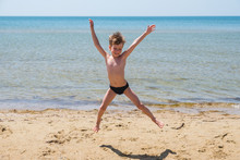 Six-year-old Boy In Black Speedo Jumping Into The Sea And Smiles.