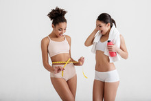 Motivated Slender Ladies Measuring Waistline After Doing Fitness. Their Faces Expressing Delight. Isolated On Background
