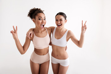 Wall Mural - Portrait of playful women enjoying their own figures. They are giving a wink at camera and showing peace sign. Isolated on background