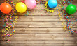 Leinwandbild Motiv Colorful carnival or party frame of balloons, streamers and confetti on rustic wooden board