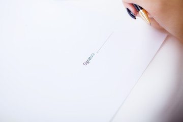 Close up girl hand putting signature on document. She situating at desk. Business concept. Low angle