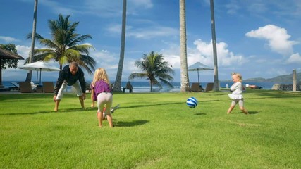father plays ball with two little daughters on green grass lawn in front of ocean