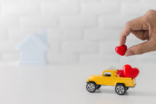 Hand Putting Red Heart In To Toy Yellow Truck Car Carrying To Home.Concept Of Happy Relationship At Home.