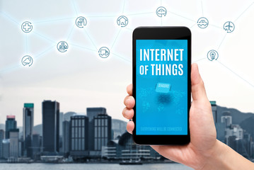 Poster - Hand holding mobile with Internet of things (iot) word on screen with icon feature glowing in air with blur city building background,Digital Lifestyle concept