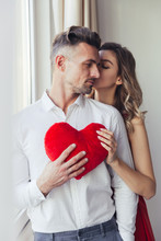 Young Gorgeous Lady In Red Dress Kiss Her Man And Holding Plush Toy Heart