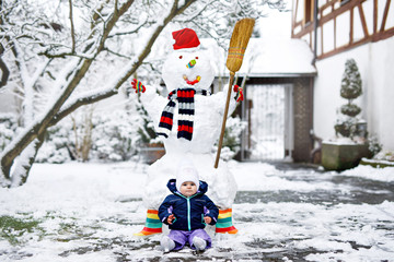 Wall Mural - Cute little beautiful baby girl on winter day with snow and snowman