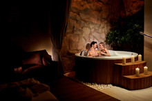 A Loving Couple With A Glass Of Champagne In A Jacuzzi With Candles Relax.