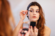 © Kalim - Attractive young woman doing make-up while looking at the mirror in bathroom