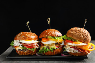 Wall Mural - Plate with tasty burgers on table against black background