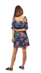 back view of standing young beautiful  woman.  girl  watching. Rear view people collection.  backside view of person.  A girl in a colorful dress watches her hands folded behind her back