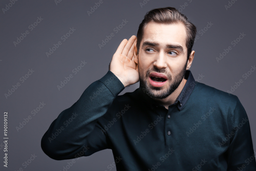 Young man with hearing problem on grey background