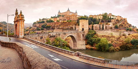Fototapete - Panorama of Old city of Toledo with Alcantara Bridge across the river Tajo and Alcazar in the overcast evening, Castilla La Mancha, Spain