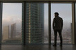 © kanashkin - Rearview of a businessman looking out the window at the city.