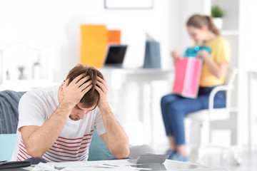 Poster - Upset man at table and woman with shopping bags in room. Money problems in relationship