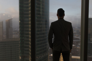 rearview of a businessman looking out the window at the city.