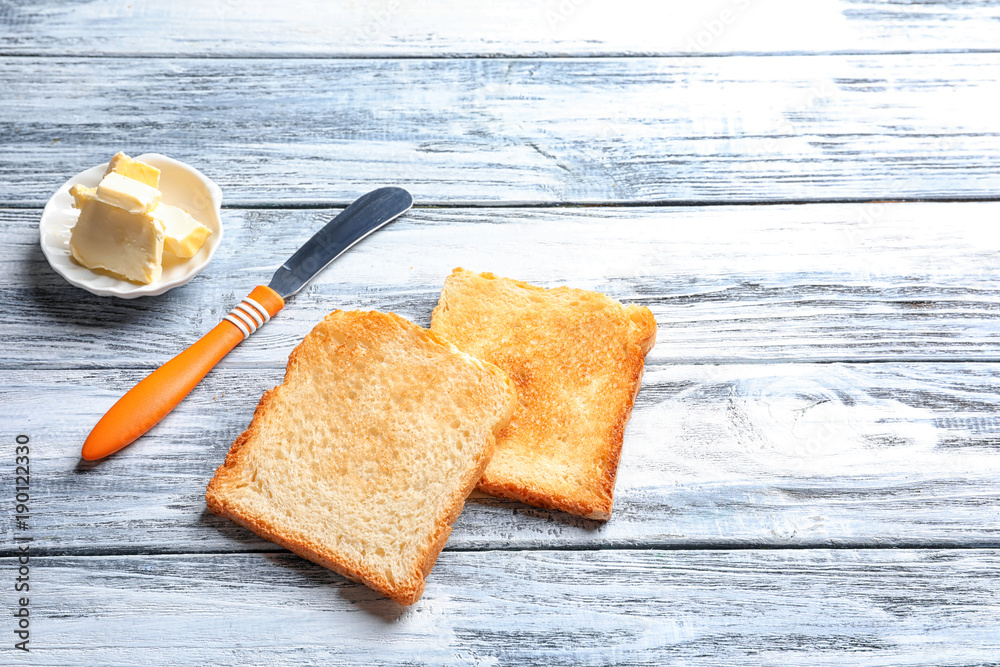 Toasted bread with knife and butter on wooden background