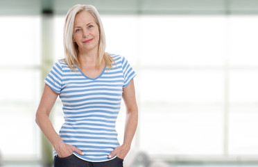Wall Mural - friendly smiling middle-aged woman is standing near the window. summer landscape outside the window 