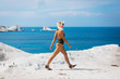 © stakhov - A sporty woman in a bikini is walking on the edge of a white mountain on the sea background.