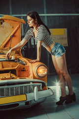 Wall Mural - Woman mechanic in sexy shorts near the vintage car