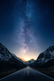 Fototapeta Góry - Milky way glowing above a road leading to distance in a mountain valley.