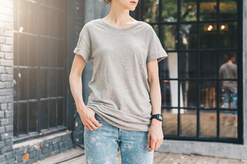 Wall Mural - Summer day. Front view. Young millennial woman dressed in gray t-shirt is stands on city street. Mock up. Space for logo, text, image. Instagram filter, film effect, bokeh effect.