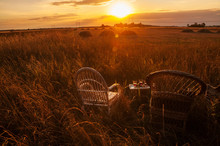 Two Wicker Chairs And A Tray With Glasses Of Wine Amid The Fields At Sunset. Beautiful Countryside. The Expanse Of Fields Rest On A Farm, Outside The City.
