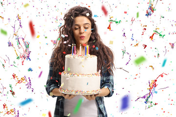 Teenage girl blowing candles on a birthday cake with confetti streamers flying around her