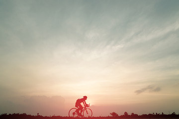 Wall Mural - Silhouette of cyclist ride bicycle on sunset background. A man Ride on bike on the road with beautiful colorful sky. Sport and active life concept.