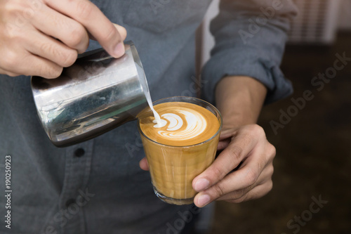 Fotografie, Obraz Close-up of male barista hand holding and pouring hot milk for prepare latte art on piccolo latte cup of coffee