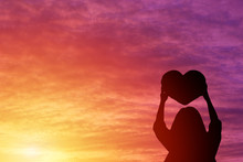 Silhouette Of A Woman Holding A Heart Shape Look At The Sky Sunset Background