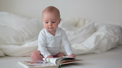 Canvas Print - Little baby boy, looking at cook with colorful pictures at home, sitting in bed