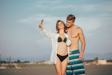 Couple Walking On Beach At Sunset Taking Selfie Picture On Mobile Phone Relaxing Together