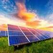 Solar panel on beautiful orange sundown background. Green grass and cloudy sky. Alternative energy concept