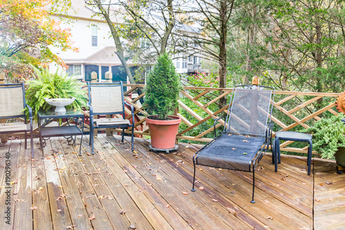 Fotografie, Obraz Closeup of wooden deck of house with many green plants, trees, tables, chairs, o