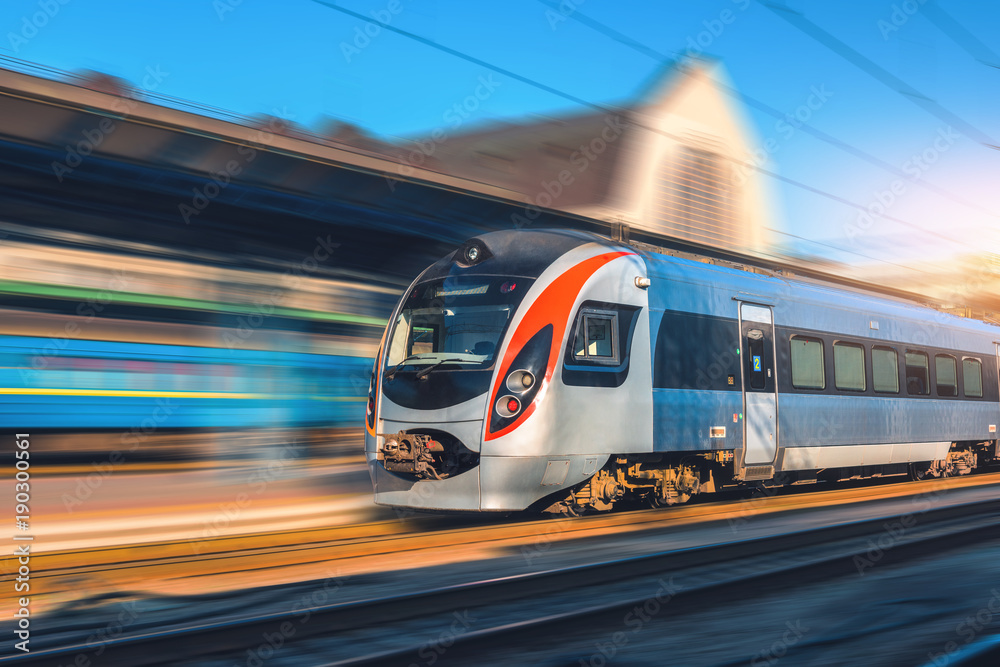High speed train in motion at the railway station at sunset in Europe. Modern intercity train on the railway platform with motion blur effect. Industrial scene with moving passenger train on railroad - obrazy, fototapety, plakaty 