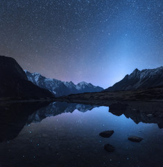 Wall Mural - Starry night in Nepal. Amazing night scene with mountains and lake. Landscape with high rocks with snowy peak and sky with stars reflected in water in Nepal. Travel in  Himalayas. Space background