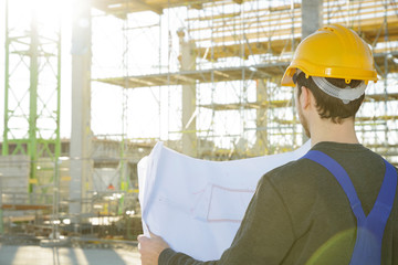 Mann in Arbeitskleidung auf einer Baustelle studiert Bau-Pläne 