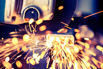 Soft focus with sparks flying from metal being bar cut with electric grinder