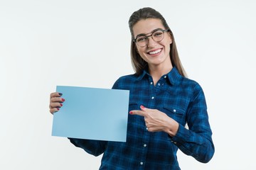 Wall Mural - Positive smiling girl student holding a cleaned sheet of blue paper, pointing a finger at the paper.