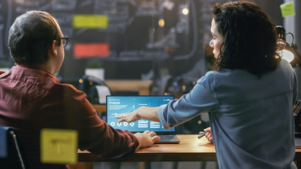 Poster - Male and Female Financiers Look at Statistics and Graphs Shown on the Laptop, They Talk Solving Problems. In the Background Creative Office.