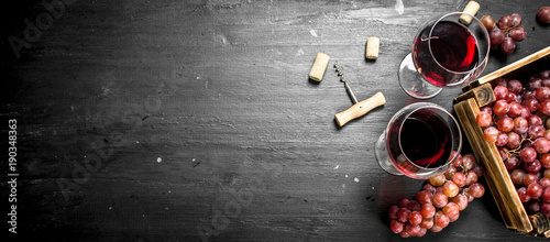 Fotografía Wine background. Red wine in an old box with a corkscrew.
