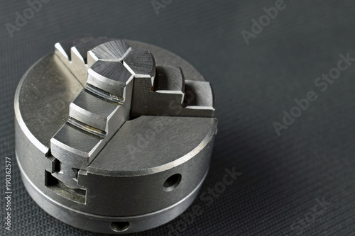 Chuck for metal lathe on dark background. Space for text. Poster