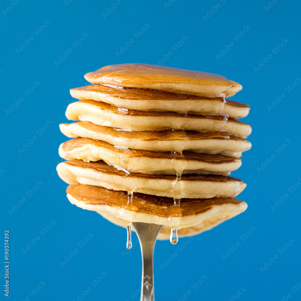 Stack of pancakes with honey decorated sweet cherry pinned on a fork on blue background - obrazy, fototapety, plakaty 