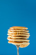 Leinwandbild Motiv Stack of pancakes with honey decorated sweet cherry pinned on a fork on blue background