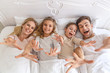 © LIGHTFIELD STUDIOS - top view of young family reaching for camera in bed