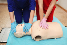 CPR. Team Doctors Works On Dummy Mannequin Indirect Cardiac Massage And Artificial Ventilation Lungs. Two Young Girls Nurse Engaged Simulator Hospital Room. Paramedics Emergency Situation