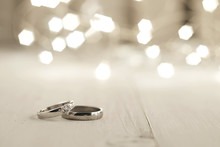 Two Wedding Rings Place On Wooden Floor With Light Bokeh Background.